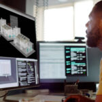 Stock image of an African American (Afro Caribbean) man working on a CAD design of a house with associated data on screen.